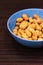 Vertical shot of a vibrant blue bowl of peanuts on a  dark brown table