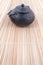 Vertical shot of vintage, black metal Japanese tea pot standing on a reed pad in a soft light. Stylish kitchen equipment.