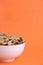 Vertical shot of a white bowl of nuts on an orange background