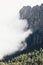 Vertical shot of a white cloud nearing the green forest and rocky mountains -perfect for wallpaper