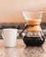 Vertical shot of a white coffee mug next to a glass coffeemaker on a kitchen table