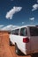 Vertical shot of a white truck driving on a sandy land under a blue sky