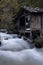 Vertical shot of a wooden cabin near a flowing waterfall in a park