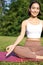 Vertical shot of young asian woman sitting on fitness mat and meditating, doing calming and relaxing exercises in park