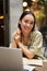 Vertical shot of young Asian woman working on remote from outdoor cafÃ©, sitting with laptop and smiling, studying