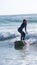 Vertical shot of a young attractive female in a wetsuit surfing at the beach