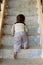 Vertical shot of a young baby boy attempting to ascend steps of staircase