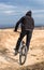 Vertical shot of a young male riding a bicycle in a brown field under blue sky