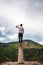 Vertical shot of a young male standing on a platform surrounded by hills under a cloudy sky