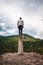 Vertical shot of a young male standing on a platform surrounded by hills under a cloudy sky