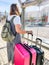 Vertical shot of a young woman with two pieces of luggage waiting at the bus stop in daylight