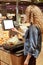 Vertical shot of young woman weighs bananas on electronic scales with touch screen, buys fruits in supermarket, stands back to cam