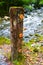 Vertical sign post with fluorescent orange markers stands in front of a rushing river