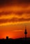 Vertical silhouette of a tower gleaming against the orange cloudy sky during sunset