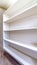 Vertical Small walk in closet with empty long cabinet shelves under slanted ceiling
