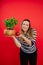 Vertical smiling plump woman in striped shirt look at camera holding green basil plant pot and juicy apple. New recipe