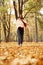 Vertical smiling, shy shivering woman, wrapped in warm plaid scarf and jumper lean on tree trunk near golden leaves area