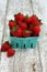 Vertical Strawberries in a green paper carton on white wood