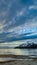 Vertical Striking cloudy sky over a calm lake that reflects the golden sun at sunset