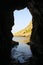 Vertical of sunlit rocky beach view from a cave, clear sky background