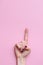 Vertical take of a hand of a caucasian woman raising the index finger on a pink background