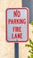 Vertical tall No Parking Fire Lane sign with a tree and wall in the background