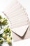 Vertical top view of a bunch of cream envelopes on white surface next to flowers