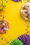 Vertical top view of plate showcasing mouthwatering donuts, extravagant masquerade mask, necklaces on yellow backdrop