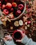 Vertical top view of a woman holding a cup of coffee with a basket full of apples on a wooden table