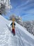 VERTICAL: Unrecognizable female snowboarder walks up a snowy hill on sunny day.