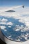 Vertical view from airborne airplane window at cloudy sky and Alps mountains with snow covered peaks at high altitude.