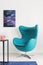 Vertical view of blue egg chair next to metal shelf with pink telephone, cosmos graphic on the wall, real photo with copy space