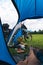 Vertical view from camp tent door. Motorcycle adventure bike on the background of green grass, forest and mountains under clouds