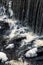 Vertical view of the foamy waves of a river flowing down the rocks in daylight in a forest