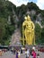 Vertical view. People in the square and climbing the stairs of the Batu Caves with the golden statue of Murugan. Malaysia