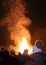 Vertical view of people standing before a roaring bonfire flames at night