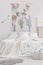 Vertical view of a scandinavian style bedroom interior with a bed dressed in white linen with painted green plants. Fabric wall ar