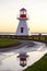 Vertical view of a small red and white lighthouse reflected in puddle