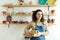 Vertical waist up portrait of young female artisan looking at camera while standing with boxes in workshop, hobby and