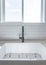 Vertical White porcelain sink with black single faucet in a kitchen against the window