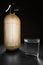 Vertical wide studio shot of backlit, luxury looking vintage soda siphon with golden color case on stone desk. Glass of