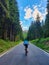 VERTICAL: Woman rides bicycle along scenic mountain road running across forest