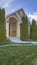 Vertical Yard and conical shaped trees at the facade of home under blue sky and clouds