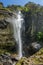 VERTICAL: Young Caucasian man hiking in Tibet poses by the stunning waterfall.