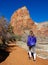 VERTICAL: Young woman treks along a dirt trail under the sandstone mountain