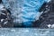 The vertically sloped  two-toned glacier tongue of Northwestern Glacier and rocks  just off the surface of the water.