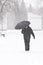 Very bad weather in a city in winter: heavy snowfall and blizzard. Male pedestrian hiding from the snow under umbrella, vertical