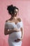 Very beautiful caucasian pregnant woman with make up and dark hair in white dress holds her belly, portrait of future