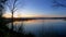 Very beautiful horizontal pan of a sunset behind a calm lake with smooth camera motion through the grass and trees on