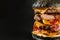 A very big black burger with three cutlets on the black background